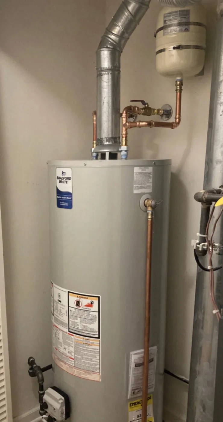 A Bradford White gas water heater installed in a closet with a galvanised flue vent, copper supply lines, a shut-off valve and a thermal expansion tank mounted above.