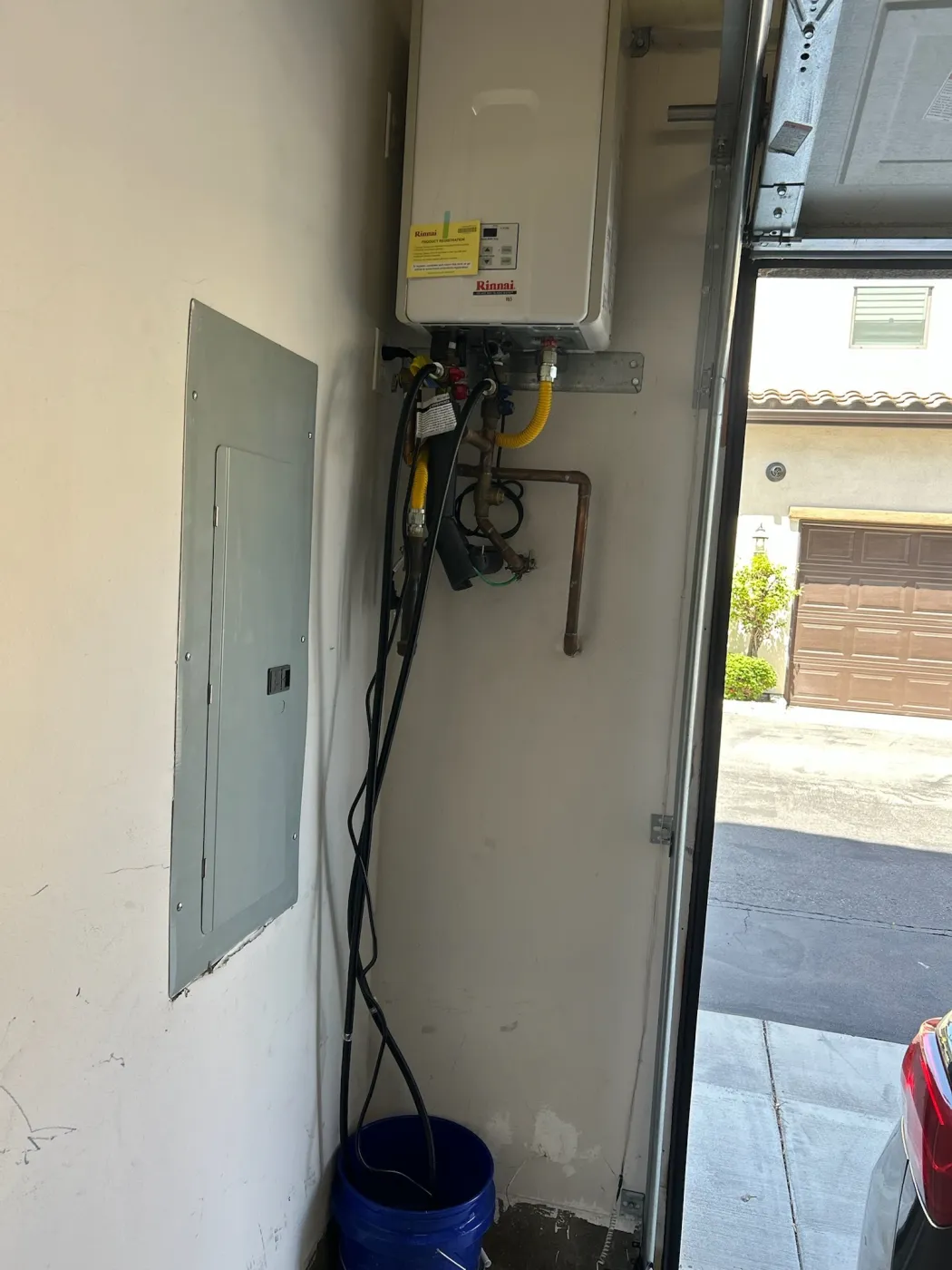 A Rinnai tankless water heater wall-mounted in a garage with a yellow flexible gas line, copper piping and isolation service valves.