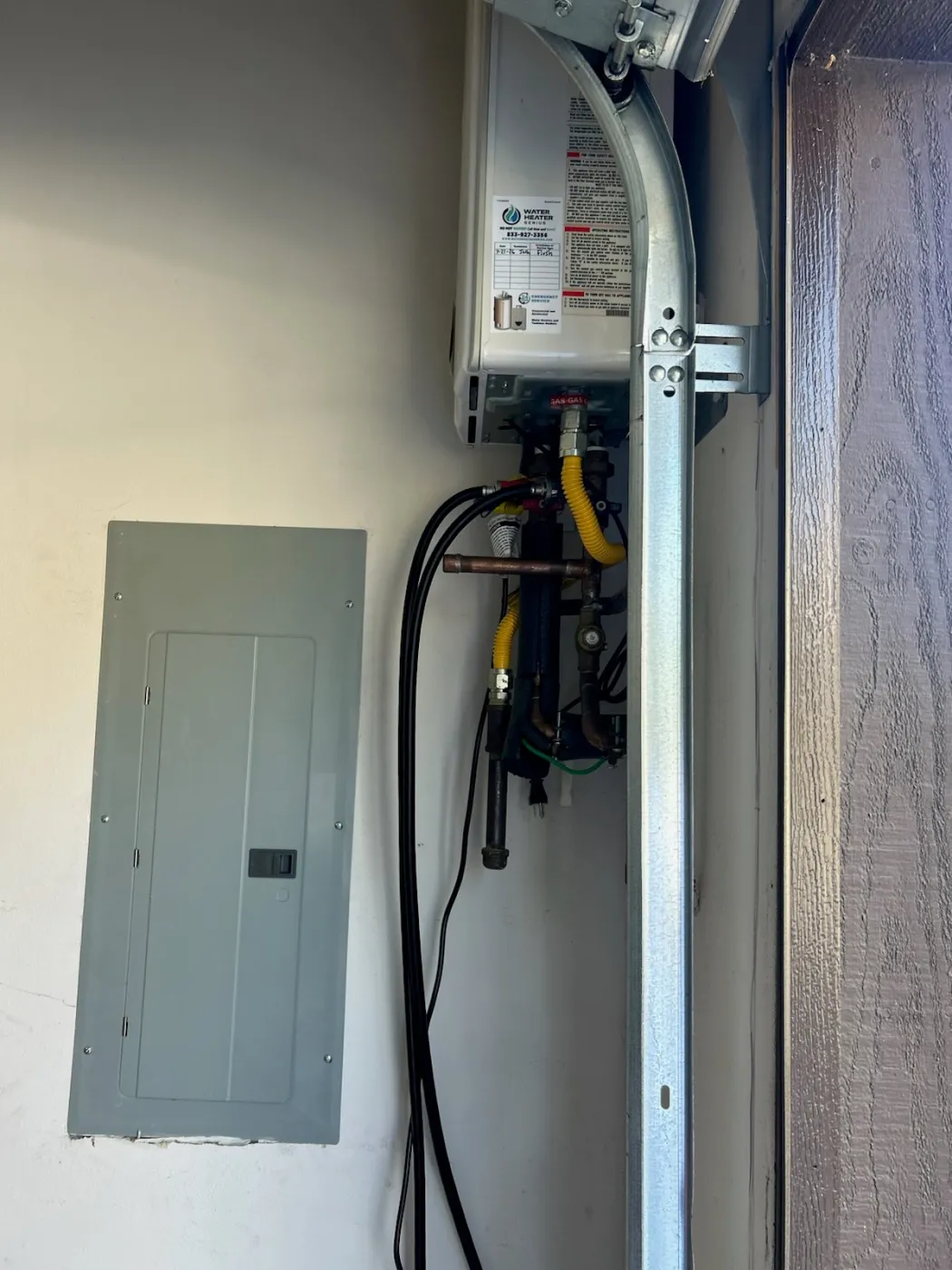 A tankless water heater carrying a Water Heater Genius service label recording the maintenance date and service phone number.